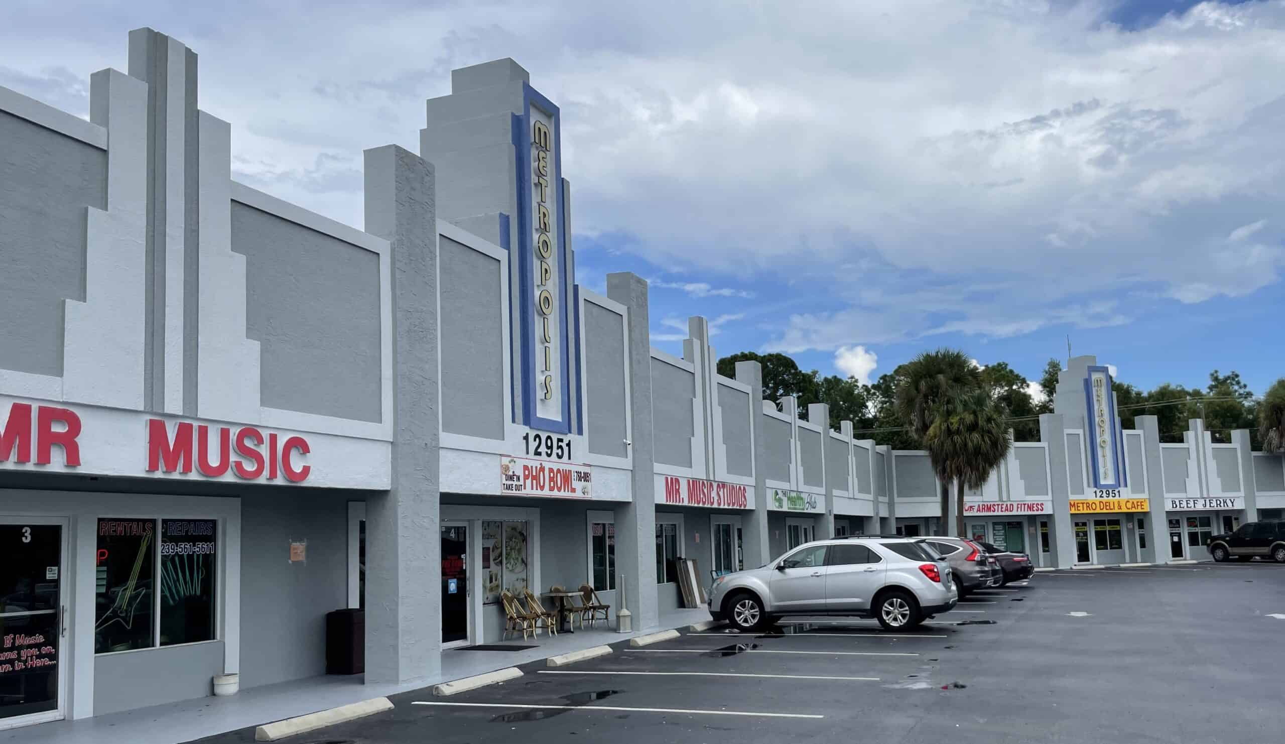 Image of a row of stores with parked cars in front of them. There are signs for Mr. Music, Pho Bon, Mr. Music Studio, Beef Jerky, and Farmstead Fitness.